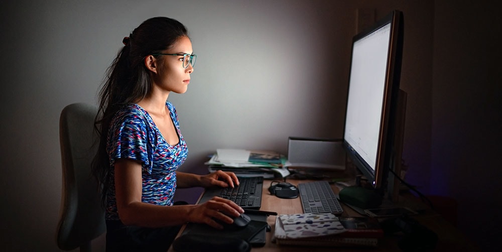 Woman in glasses sitting in front of bright computer screen
