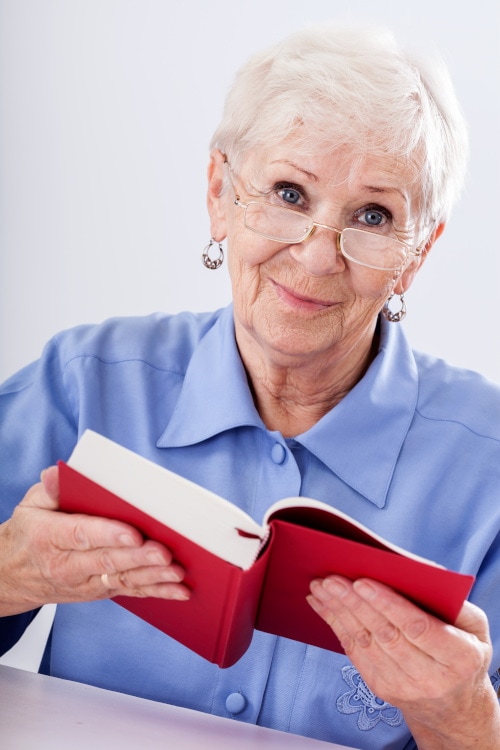 Elderly woman in glasses smiling while reading a book