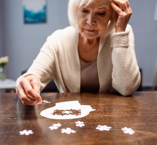Elderly woman struggling to complete a brain-shaped puzzle.