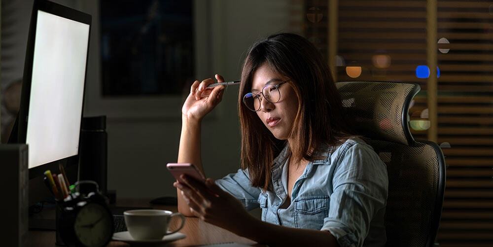Woman looking at phone screen in front of computer monitor