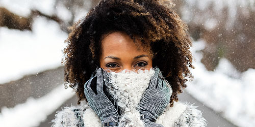 Close-up of woman wearing warm gloves and winter coat in snowy outdoors, emphasizing eye health.