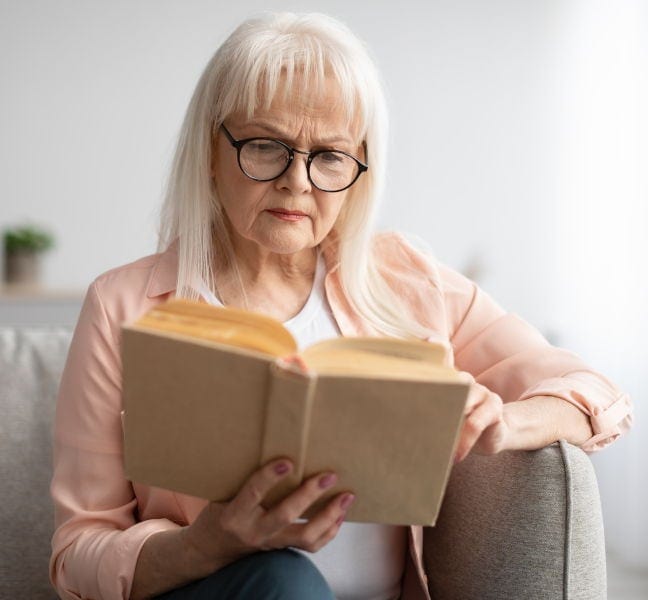 Elderly woman reading a book with glasses, at Assil Gaur Eye Institute.
