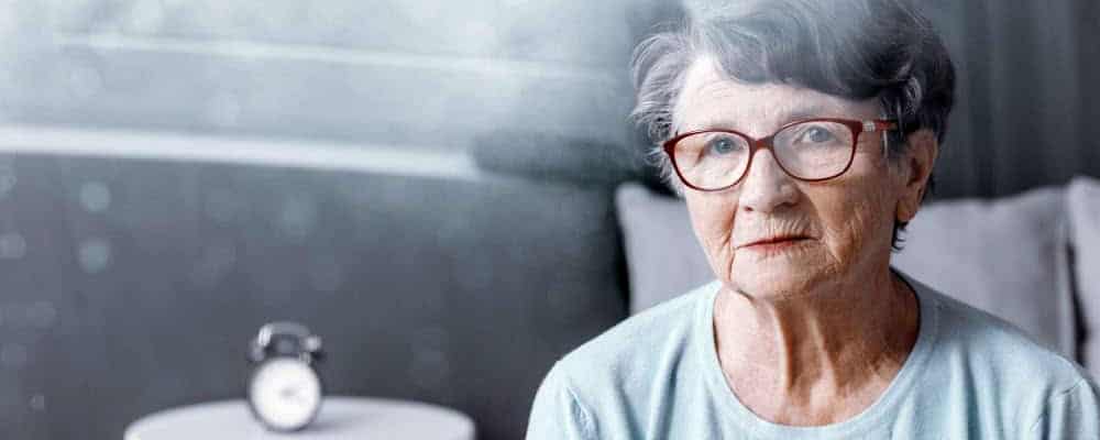 Elderly woman with glasses sitting indoors, reflecting on eyesight and health.