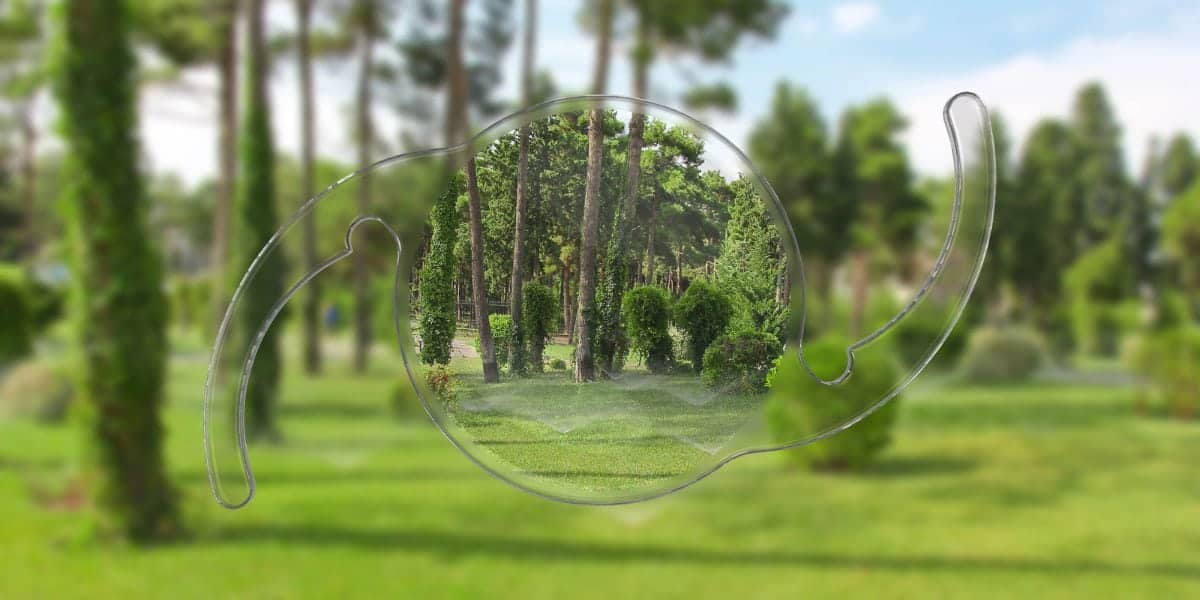 Photo of a transparent eye-shaped glass against a green park background.