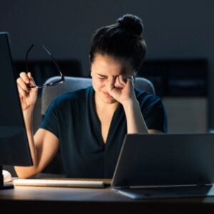 Woman experiencing eye discomfort at her desk, highlighting dry eye issues.