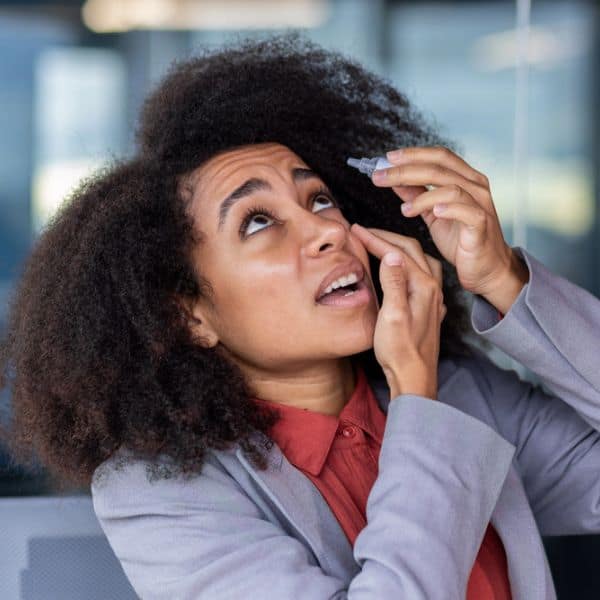 Woman with curly hair applying eye drops for dry eye relief at clinic.