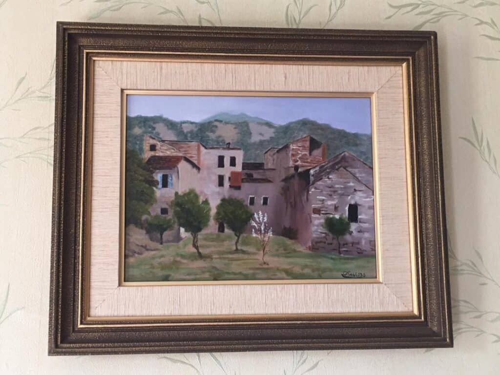 Watercolor painting of a rustic village with trees and mountains in the background.