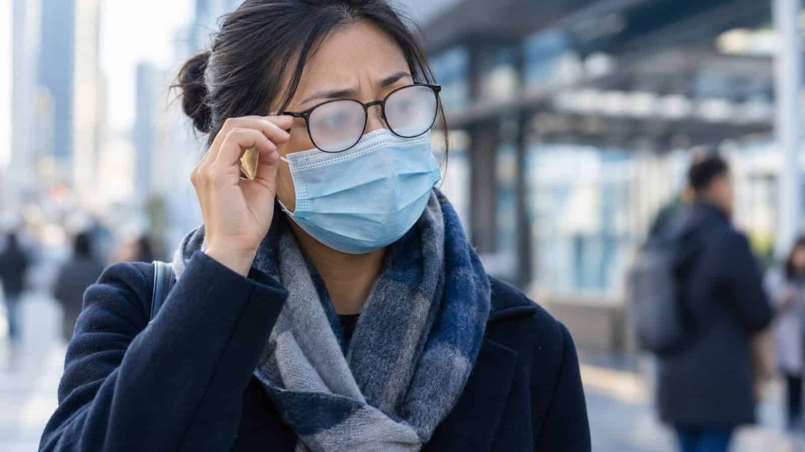 Woman with glasses and face mask adjusting her glasses outdoors.